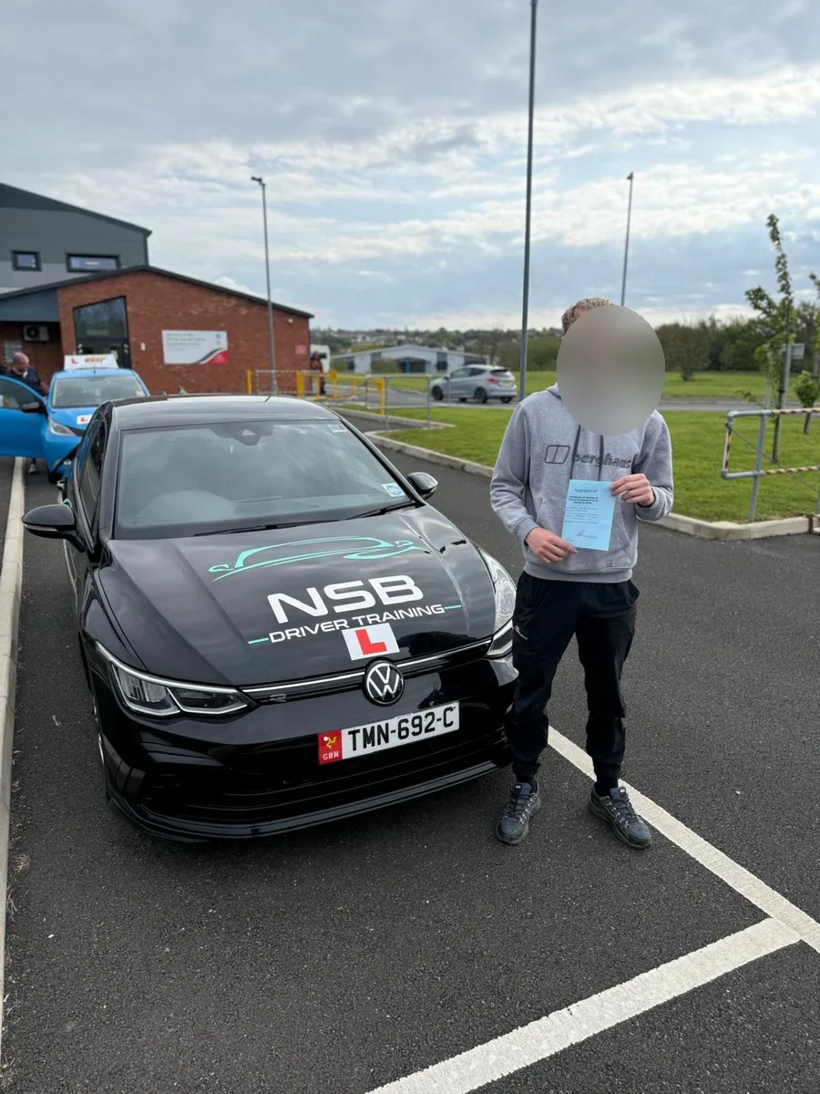 An anonymised learner holding a pass certificate beside the branded NSB Driver Training car