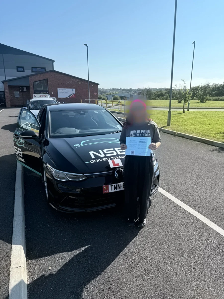 An anonymised learner celebrating test-day success beside the branded NSB Driver Training car